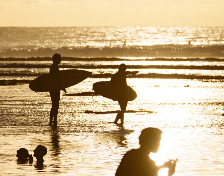 Two surfers carrying boards into golden evening light